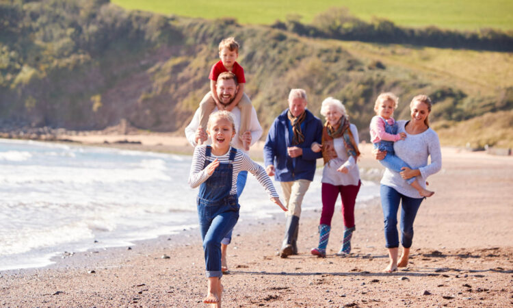 Multi-Generation Family Walking Along Shoreline Of Beach By Waves Together